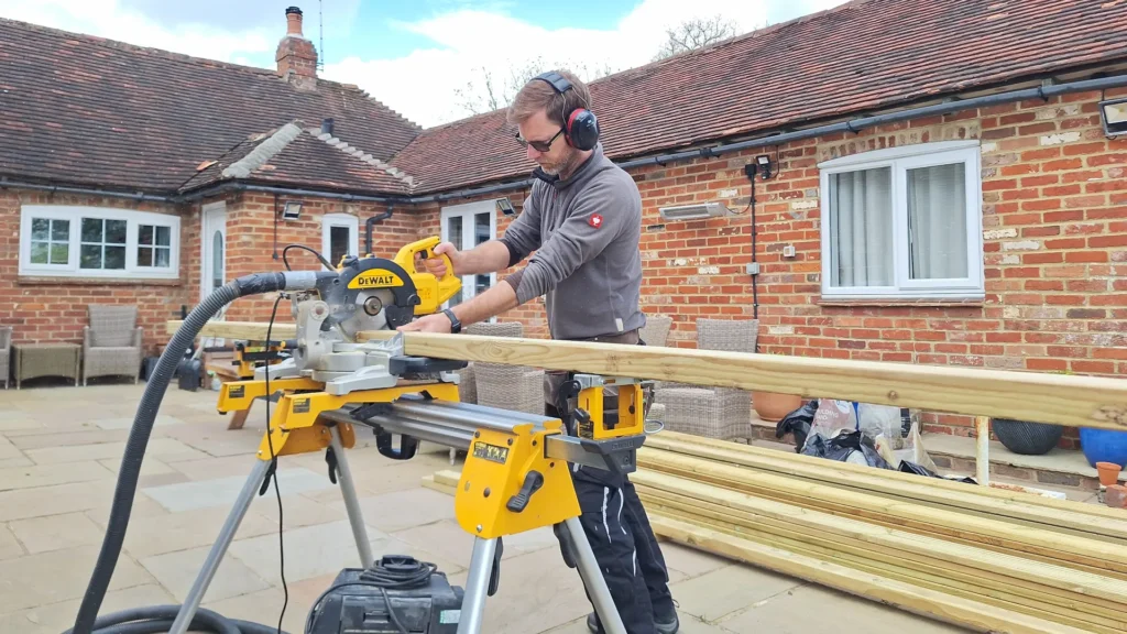Professional carpenter using a DeWalt compound mitre saw to cut timber for a decking project.
