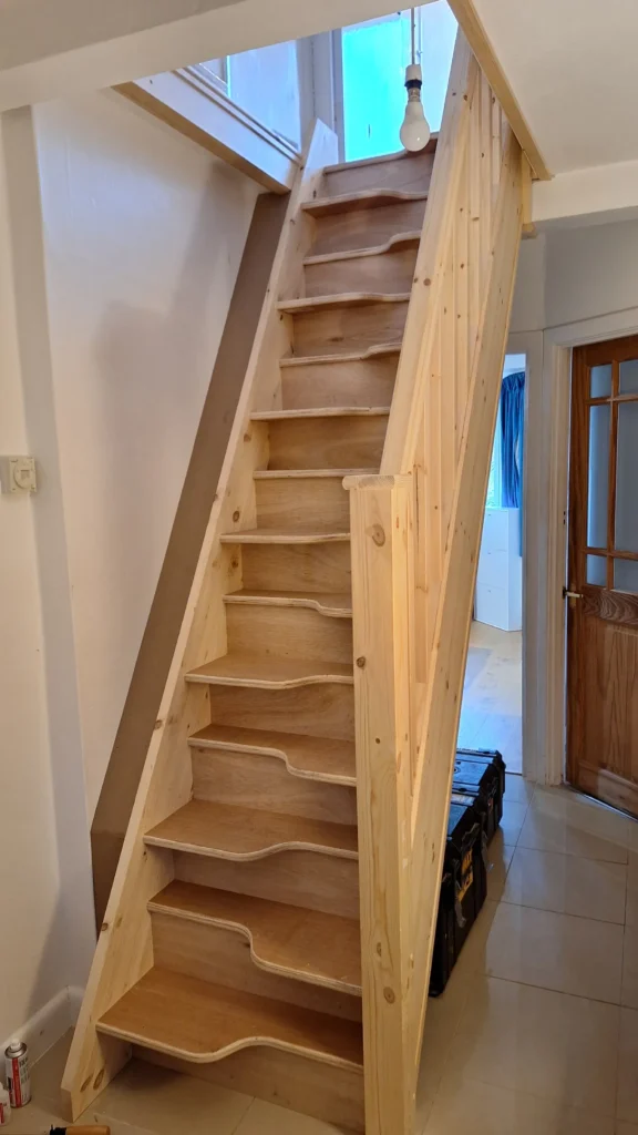 Installation of unpainted timber loft stairs featuring a natural wood handrail and spindles and plywood treads custom-fitted for a home loft conversion in Bexhill-on-sea
