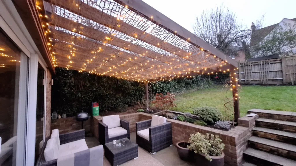 Bespoke timber pergola installation with decorative fairy lights, featuring heavy-duty support posts and a classic slatted roof design for an illuminated garden seating area.