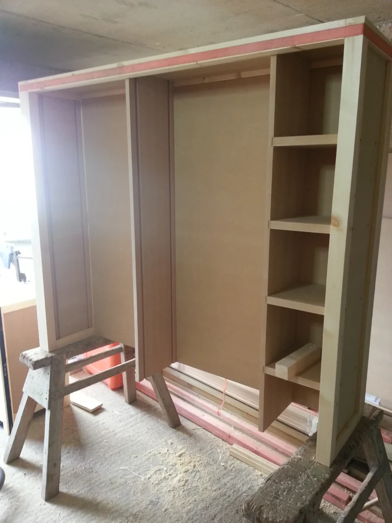 Large timber and MDF bookshelf frame under construction on sawhorses, showing the tall vertical shelving layout.