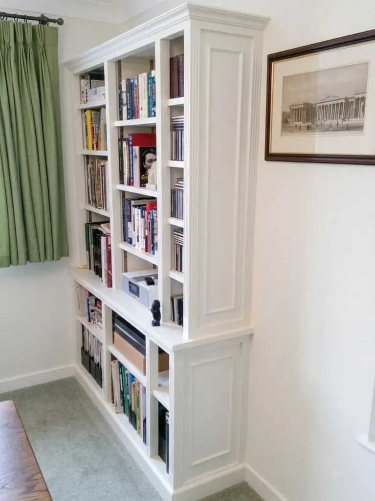 The completed bespoke library cabinet with fluted pilasters and decorative cornicing, now finished in a clean white paint and fully loaded with books and CD's in a client's home.