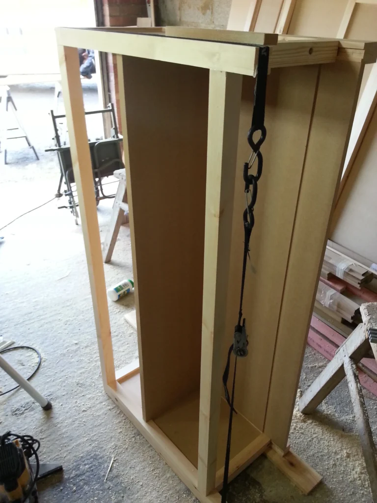 The internal carcass of the bespoke cabinet being assembled and held vertically with a ratchet strap.