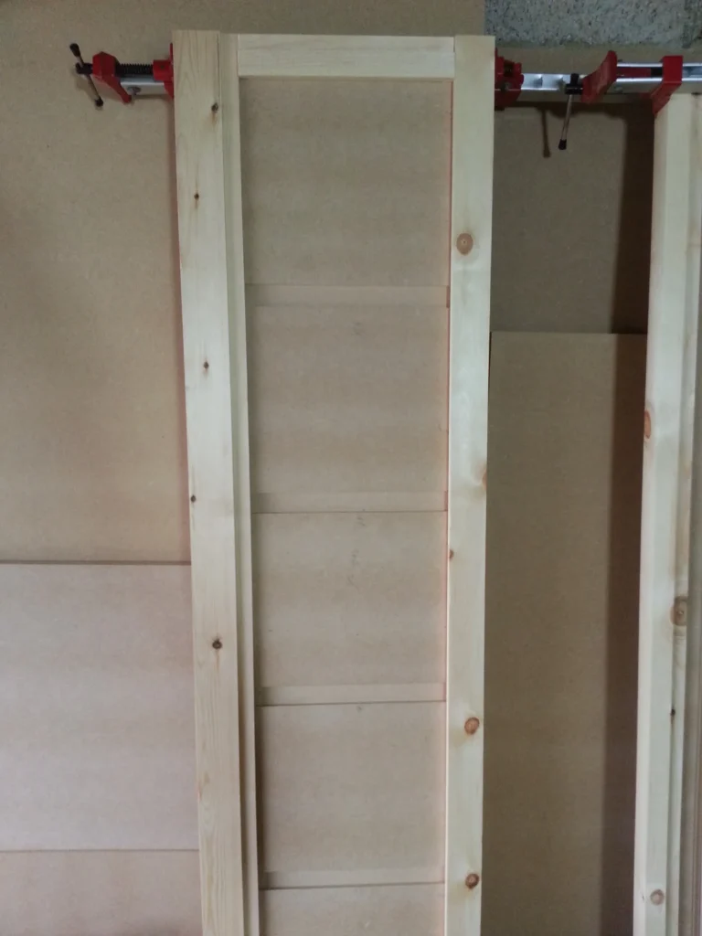 Custom timber cabinet frame being glued and held in place with red sash clamps.