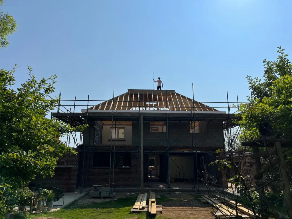A professional carpenter standing on a newly constructed cut and pitch timber roof carcass during a large-scale residential building project.