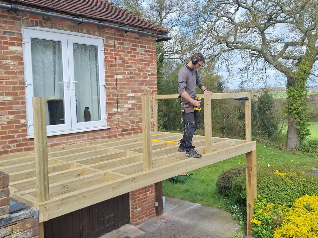 A professional carpenter installing structural timber joists and balustrade posts for a bespoke elevated garden deck.