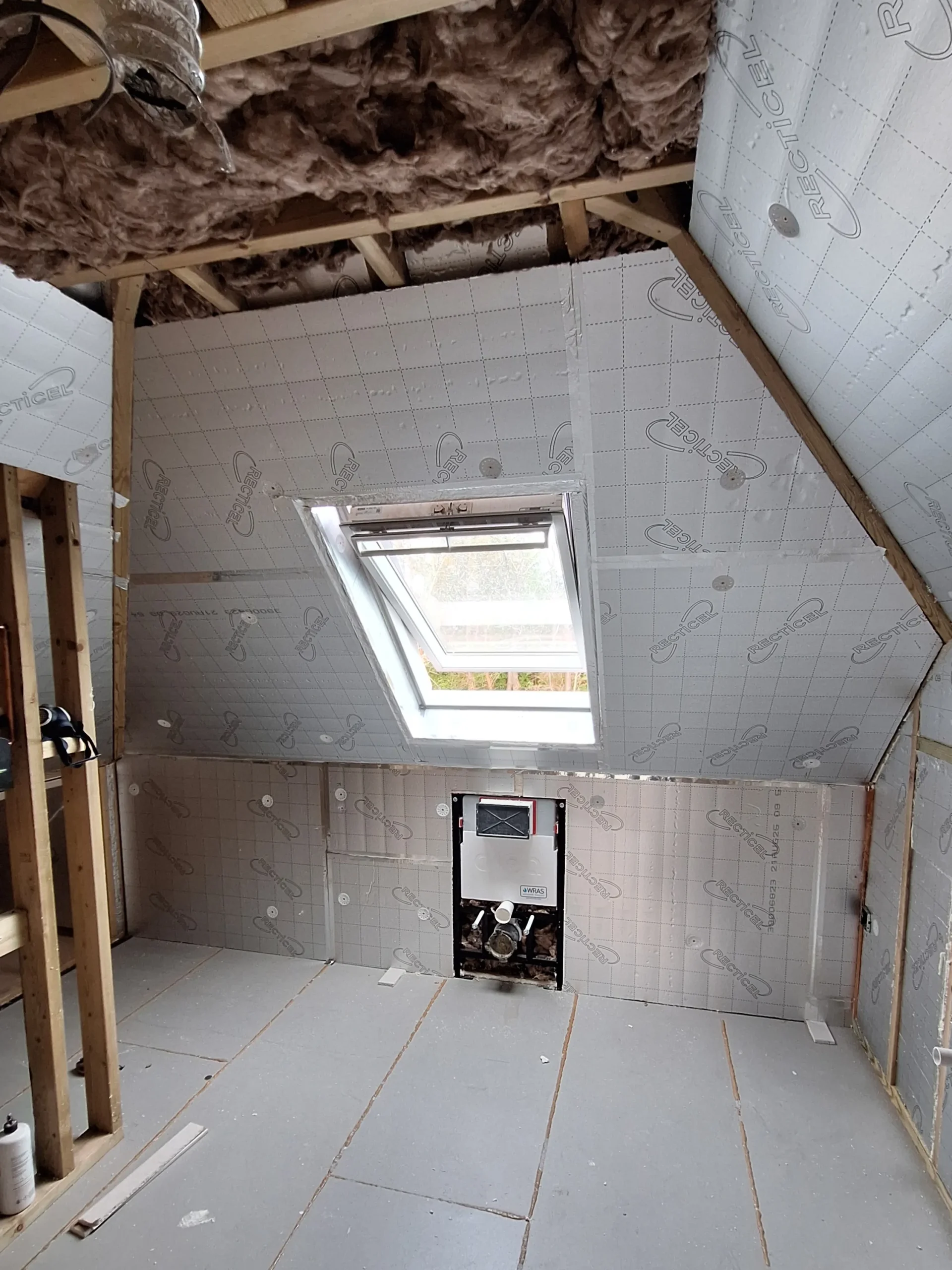 A loft conversion in progress, featuring structural timber framing, high-performance Celotex insulation, and a newly installed Velux roof window.