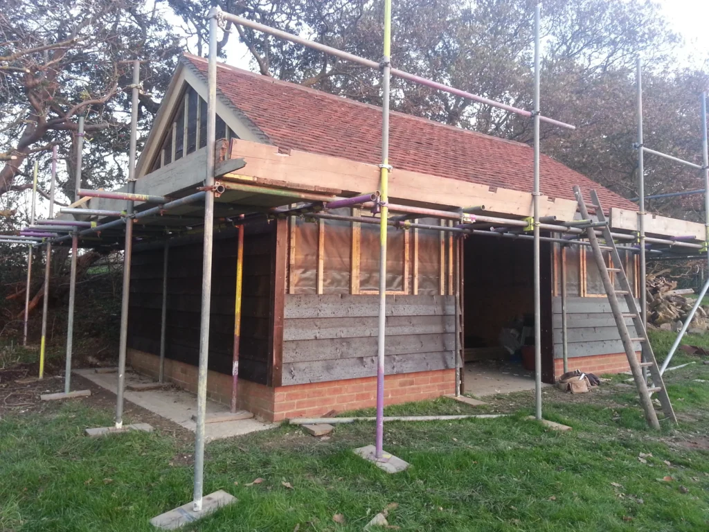 Work-in-progress shot under scaffolding, showing the installation of dark timber weatherboard cladding over a breathable membrane.