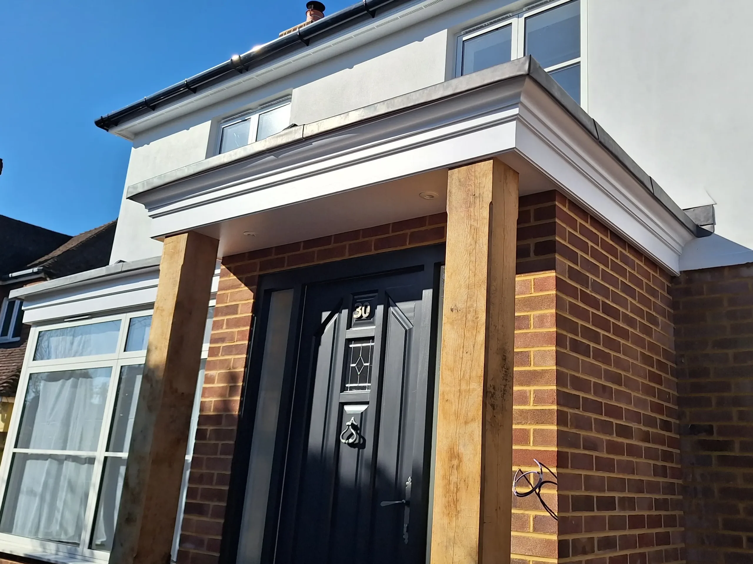 A bespoke front porch featuring solid oak support posts and a traditional white cornice roof finish over a modern front door.