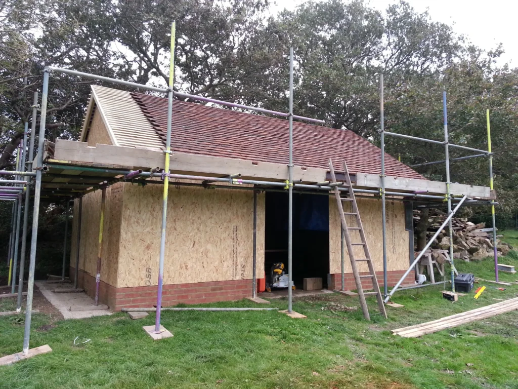View of the roof construction featuring traditional clay tiles being laid over a timber batten and OSB sheathing.