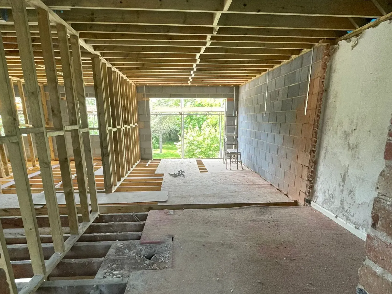 Extensive first-fix structural carpentry for a home extension, showing newly installed timber floor joists, stud wall framing, and ceiling joists.