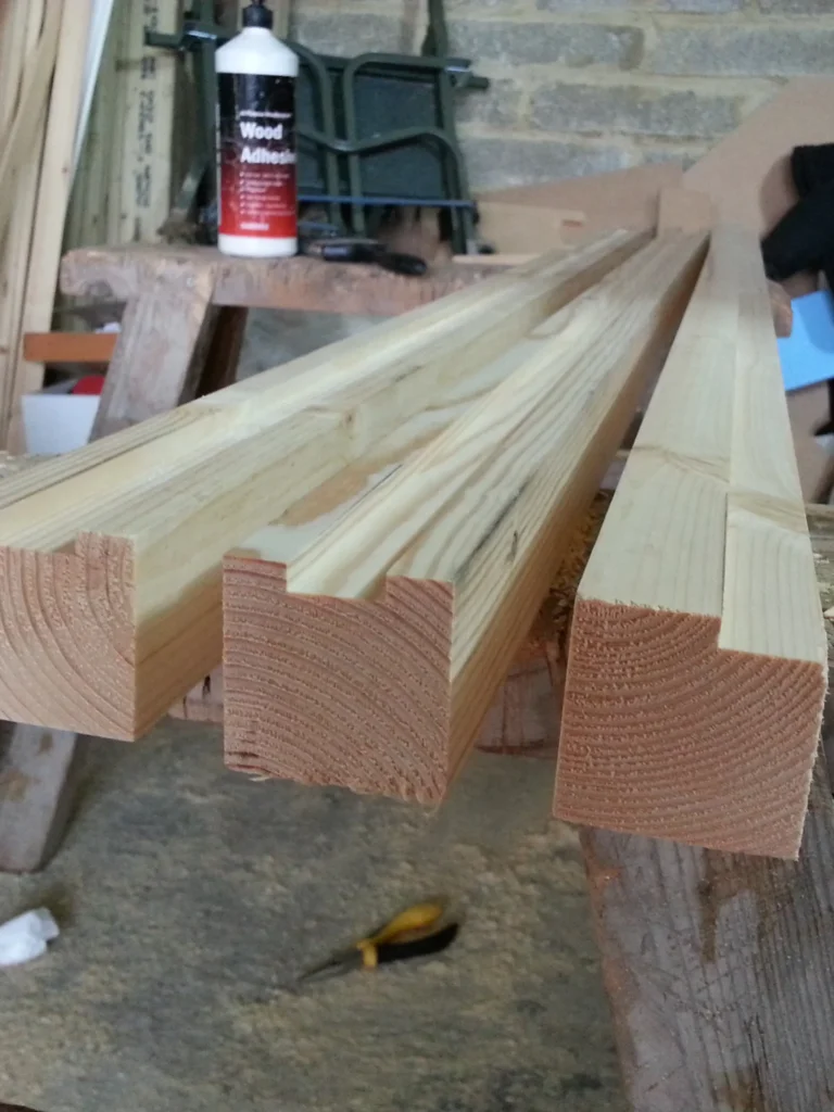 Close-up of structural timber lengths with precision-cut rebates on a workbench in a workshop.