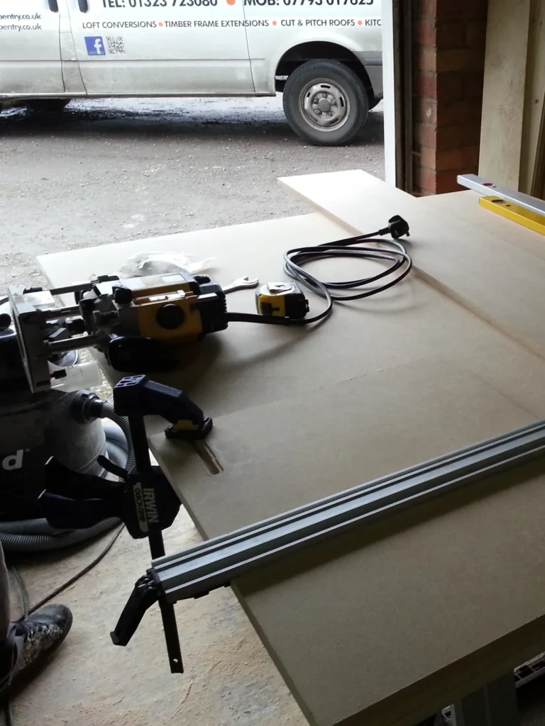 Workshop station with a plunge router, straight edge guide, and vacuum extraction system prepared for cutting MDF panels.